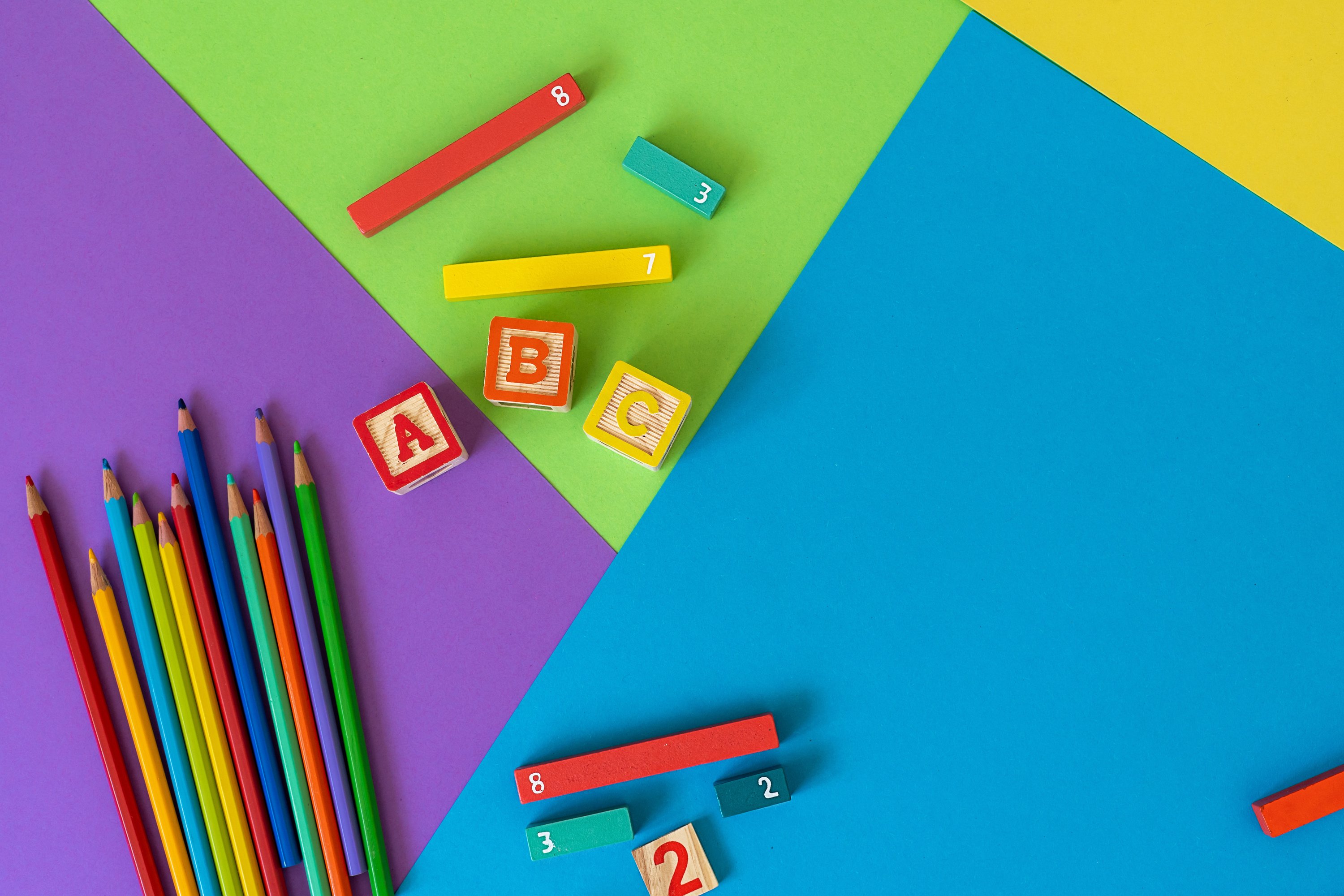 Wooden kids toys on colourful paper. Educational toys blocks, fractions, pencils, numbers. Toys for kindergarten, preschool or daycare. Back to school background. Top view